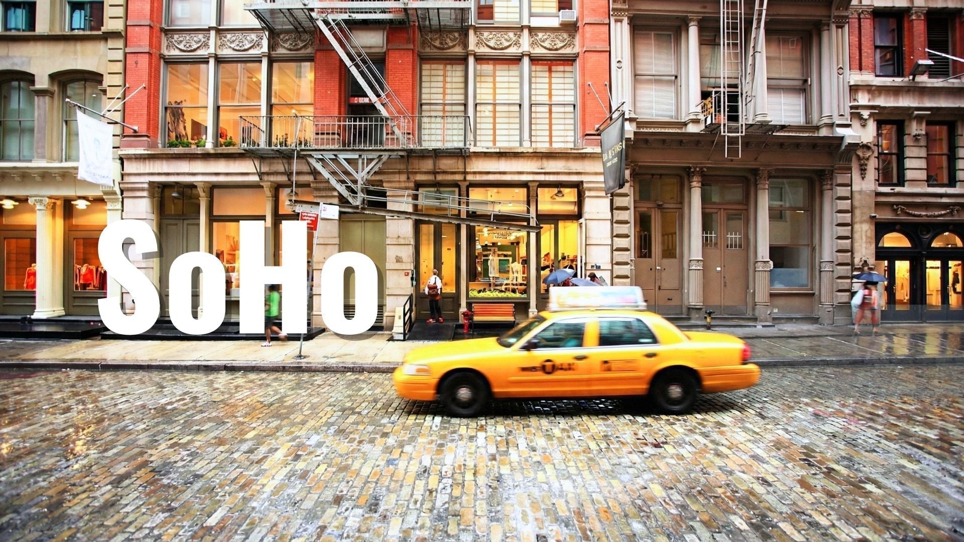Yellow taxi driving on wet cobblestone street in SoHo, New York City with historic buildings