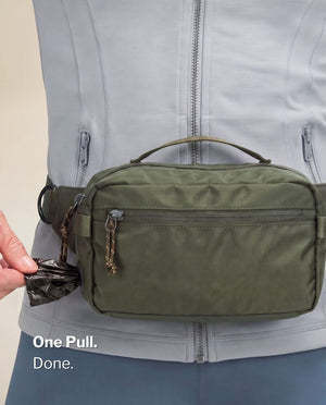 Pulling a fresh poop bag from the side dispenser port of the olive green SUSU Grab & Go dog walking bag worn on the waist