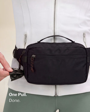 Pulling a fresh poop bag from the side dispenser port of the black SUSU Grab & Go dog walking bag worn on the waist