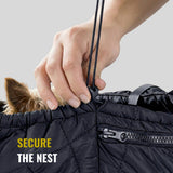Hand cinching a quilted black pet carrier sling with a small dog's ears visible inside