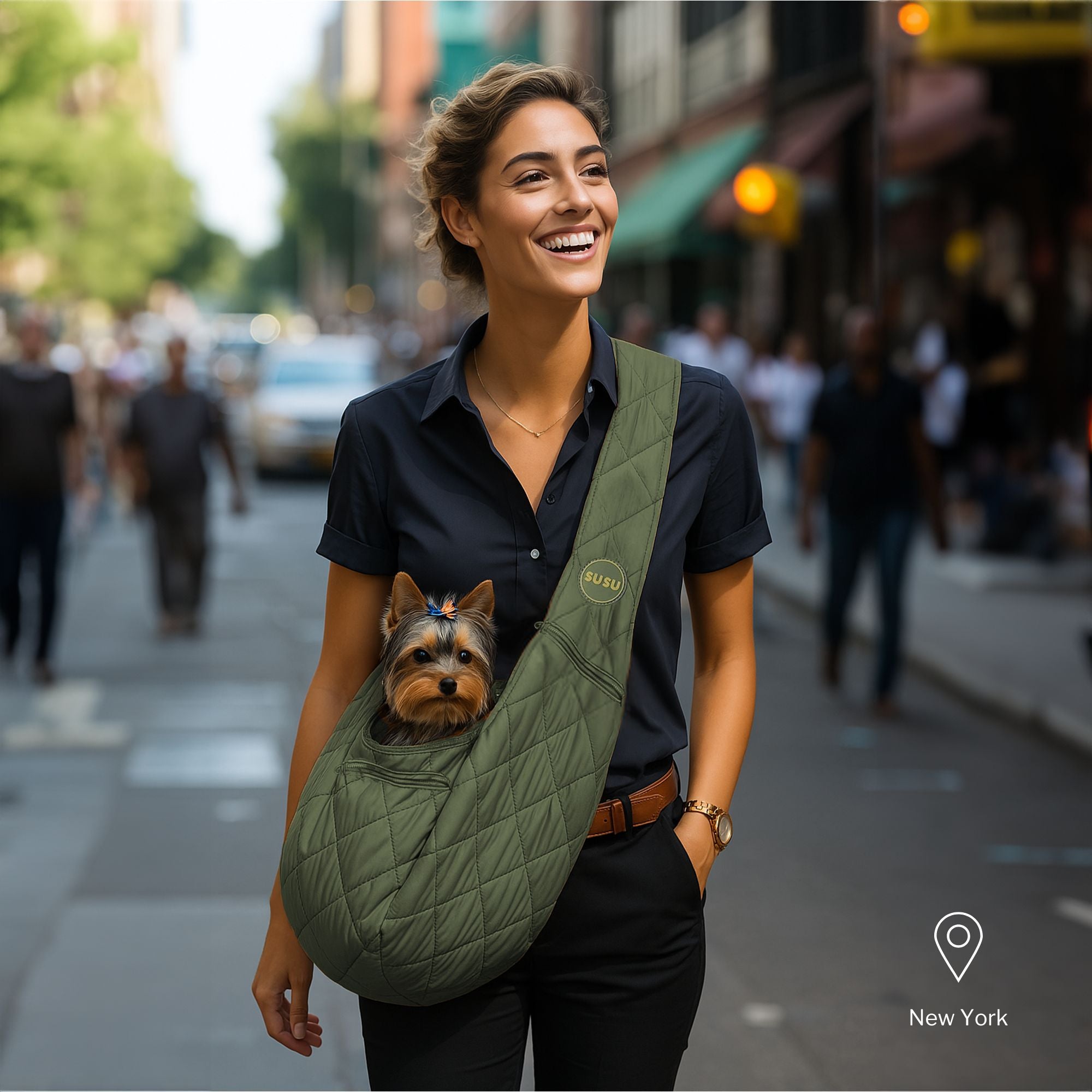 Smiling woman walking down a busy New York street carrying a small Yorkie in an olive green SUSU quilted pet carrier sling bag.