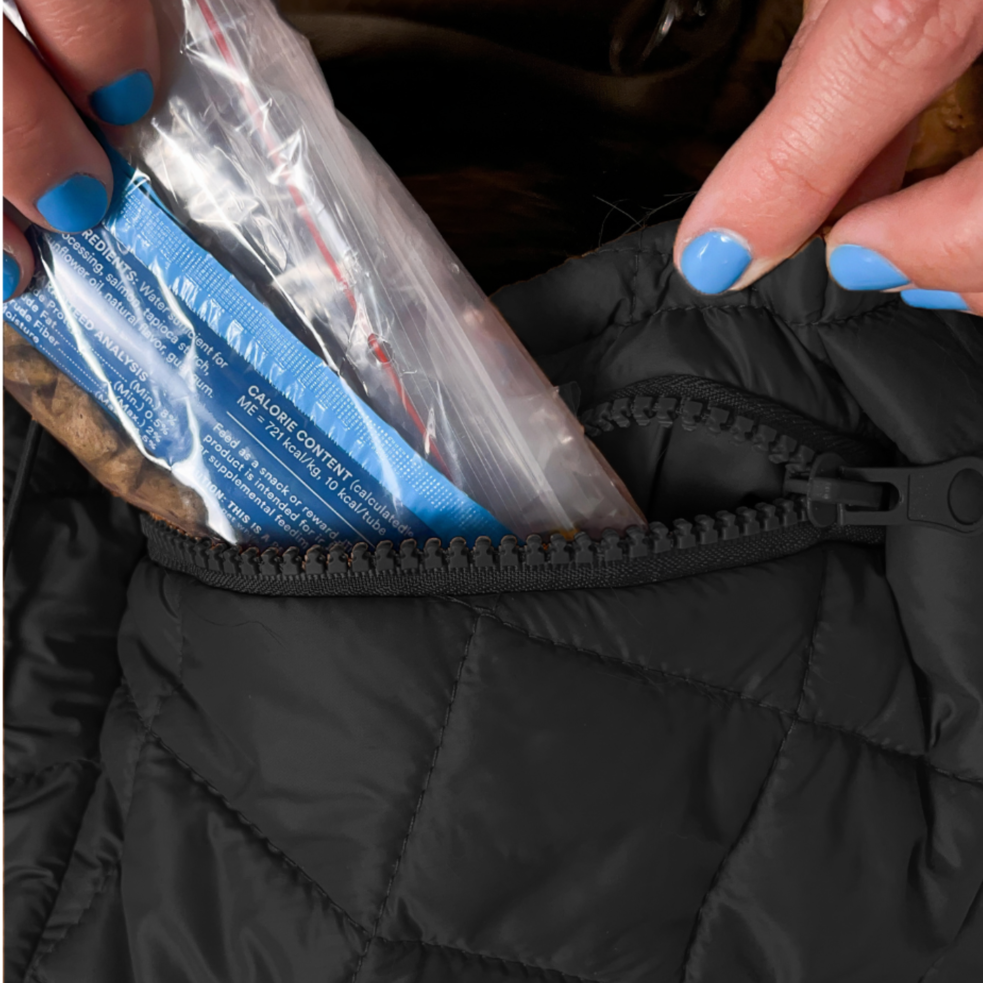 Hand placing dog treats into the zippered pocket of the black SUSU Sling small dog carrier